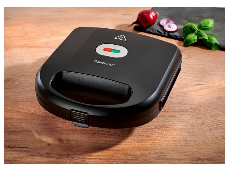 Czarny opiekacz SilverCrest na drewnianym stole z cebulą i bazylią.