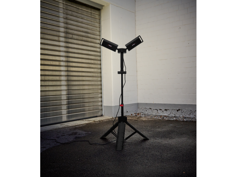 Lampa robocza z dwoma reflektorami na statywie przy bramie garażowej.