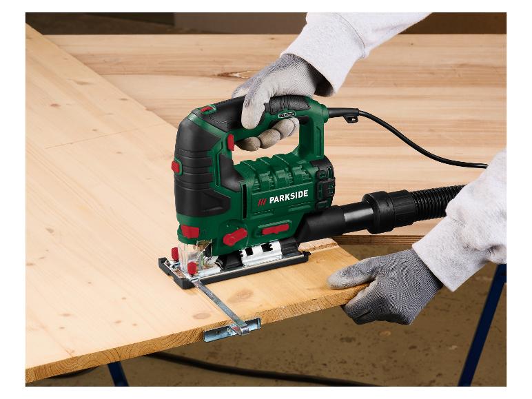 Osoba tnie deskę drewnianą wyrzynarką elektryczną, w rękawicach ochronnych.