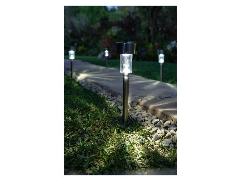 Lampy solarne ogrodowe oświetlające kamienną ścieżkę o zmierzchu.