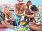 Grupa osób piknikuje na plaży, korzystając z chłodnicy i kolorowych naczyń.