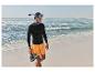 Mężczyzna w czarnej koszulce rashguard i pomarańczowych szortach z maską do snorkelingu i butami do wody na plaży