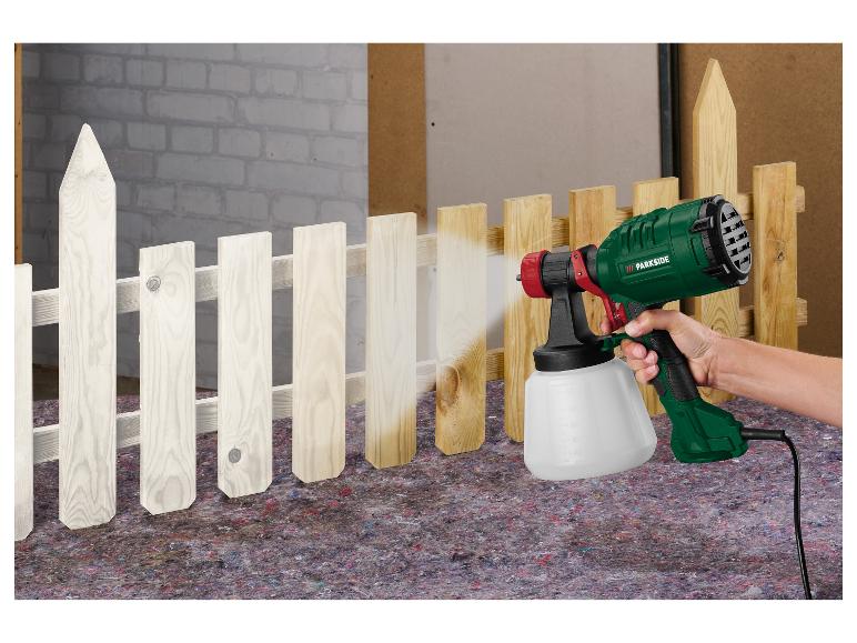 Osoba malująca drewniany płot na biało pistoletem natryskowym Parkside.