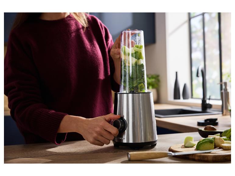 Kobieta używa blendera z owocami i warzywami do przygotowania smoothie w kuchni.