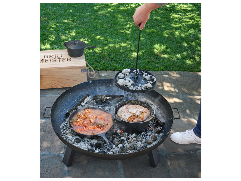 Żeliwna patelnia z krewetkami i żeliwny garnek z chlebem nad ogniem w palenisku.