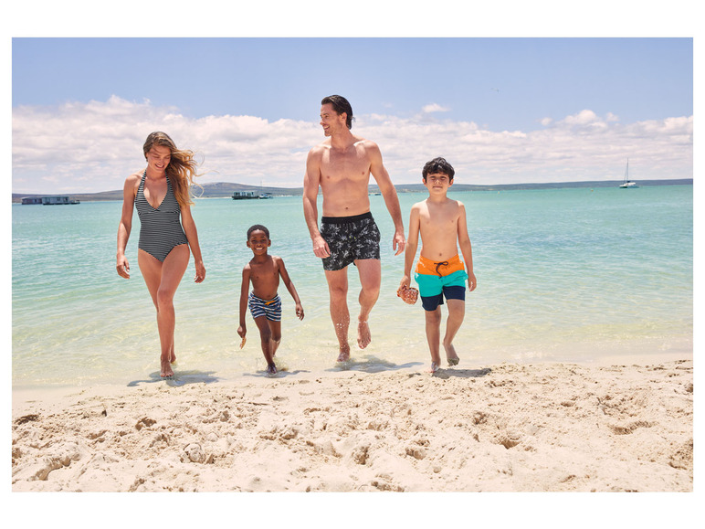 Rodzina w strojach kąpielowych idzie po piaszczystej plaży.