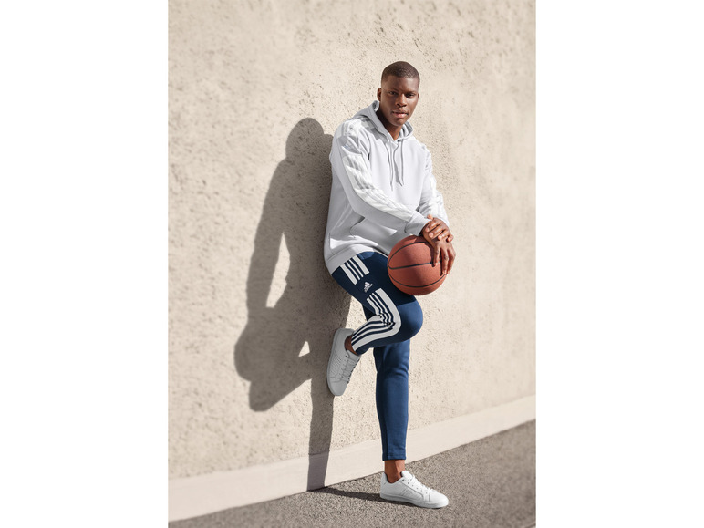 Mężczyzna w bluzie i spodniach Adidas z piłką do koszykówki