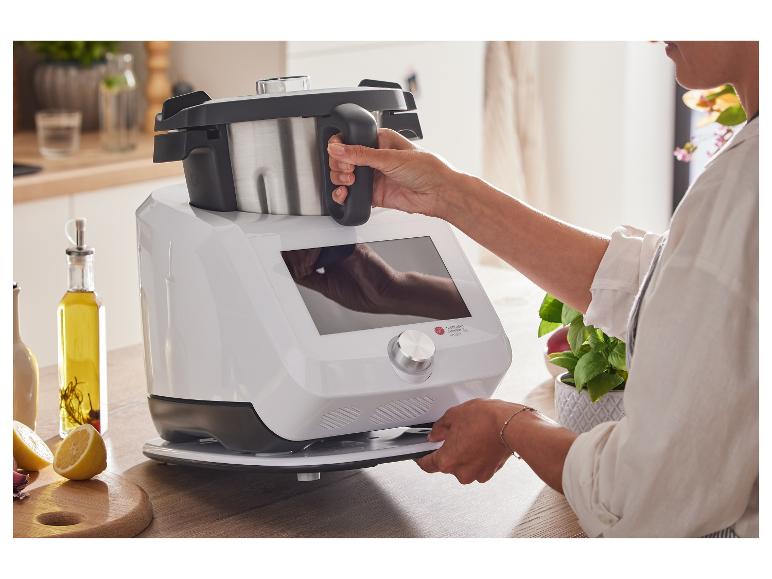 Kobieta obsługuje biały robot kuchenny z misą ze stali nierdzewnej w jasnej kuchni.