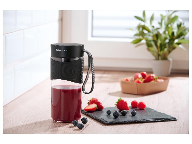 Przenośny blender SilverCrest z czerwonym koktajlem i świeżymi owocami na drewnianej desce.