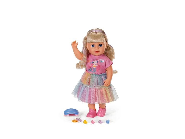 Lalka BABY born z blond włosami, różowym topem, tęczową spódniczką i akcesoriami.