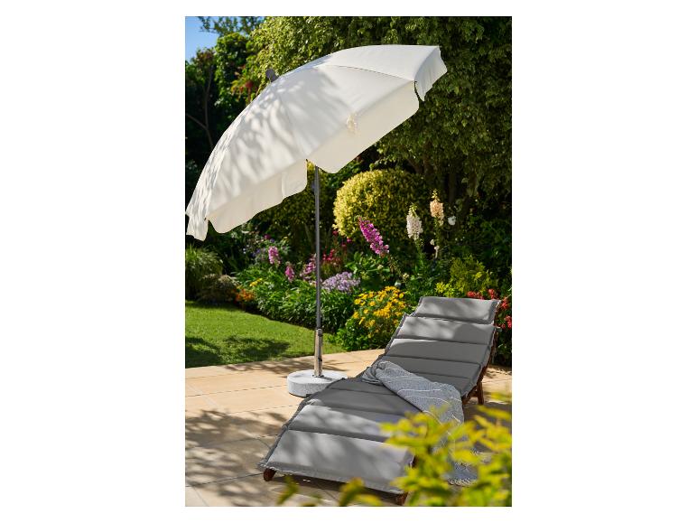 Biały parasol ogrodowy i szary leżak z niebieskim kocem na patio.