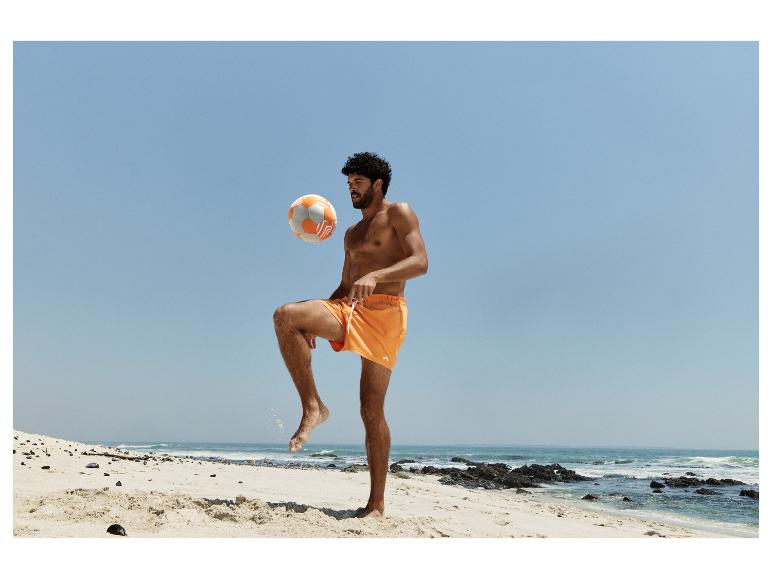 Mężczyzna w pomarańczowych szortach kąpielowych gra w piłkę plażową na piaszczystej plaży.