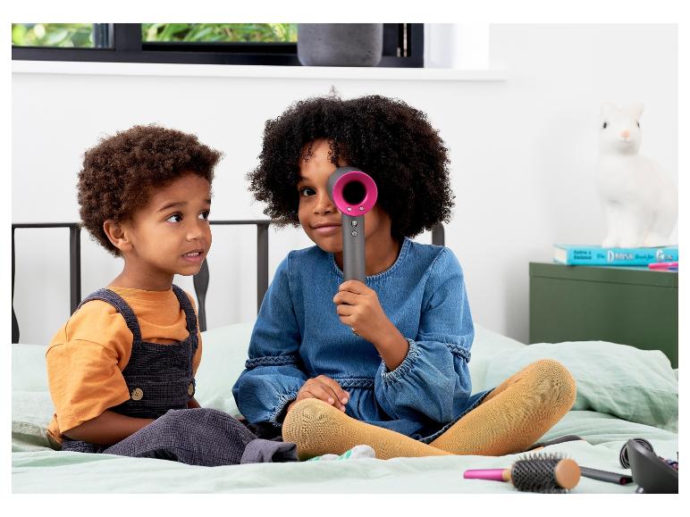 Dzieci bawią się suszarką do włosów Dyson i grzebieniami.