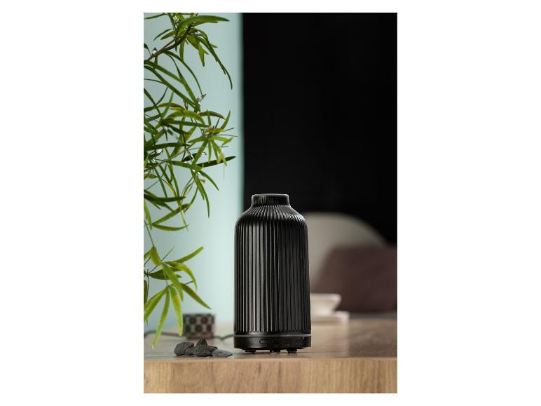 Czarny ceramiczny dyfuzor olejków eterycznych na drewnianej powierzchni obok rośliny.