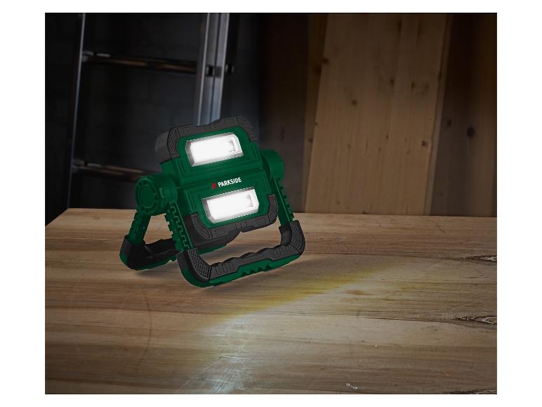 Zielona lampa robocza PARKSIDE na drewnianej powierzchni, ze snopami światła