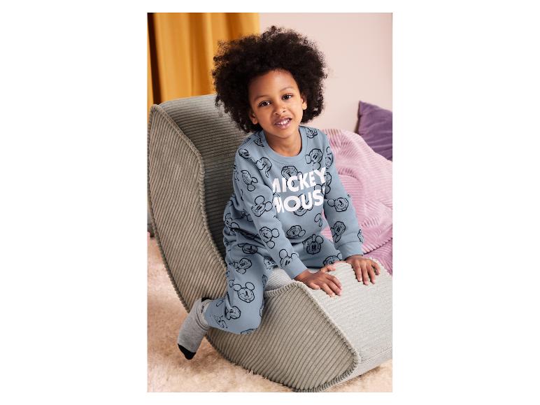 Dziecko w jasnoniebieskim dresie Myszki Miki, siedzące na szarym prążkowanym siedzisku.