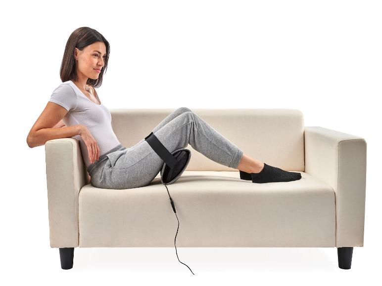 Kobieta siedzi na białej sofie z poduszką masującą na nodze.