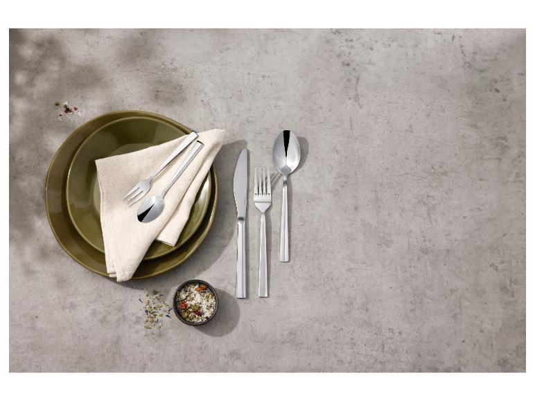 Zestaw sztućców ze stali nierdzewnej, talerze i przyprawy na szarym tle.