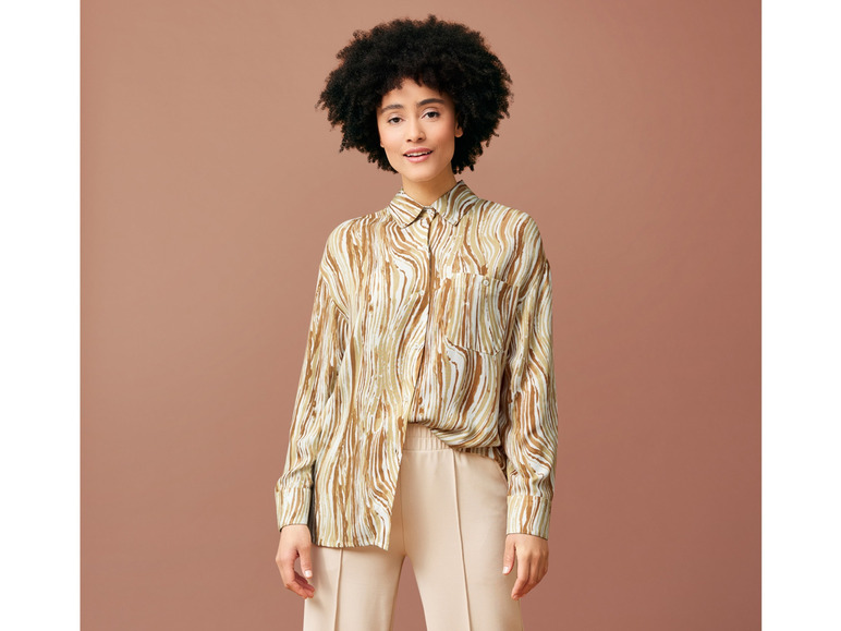 Kobieta w beżowych spodniach i koszuli z abstrakcyjnym wzorem.