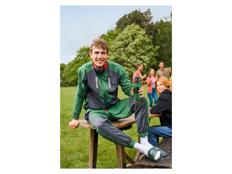 Uśmiechnięty mężczyzna w zielono-szarej kurtce PARKSIDE® siedzący na świeżym powietrzu.