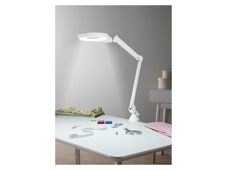 Biała lampa biurkowa z lupą i akcesoriami do szycia na białym stole.