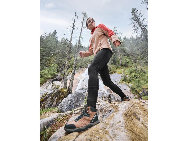 Kobieta w kurtce i spodniach wędruje po skalistym terenie.