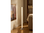 Cylindryczna lampa podłogowa z chromowaną podstawą oświetla nowoczesny salon z regałem i sofą.