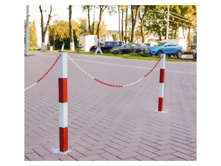 Czerwono-białe słupki z łańcuchem na ulicy z zaparkowanymi samochodami.