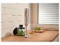 Blender ręczny ze stali nierdzewnej z drewnianymi akcentami, przygotowujący pesto na drewnianym blacie.