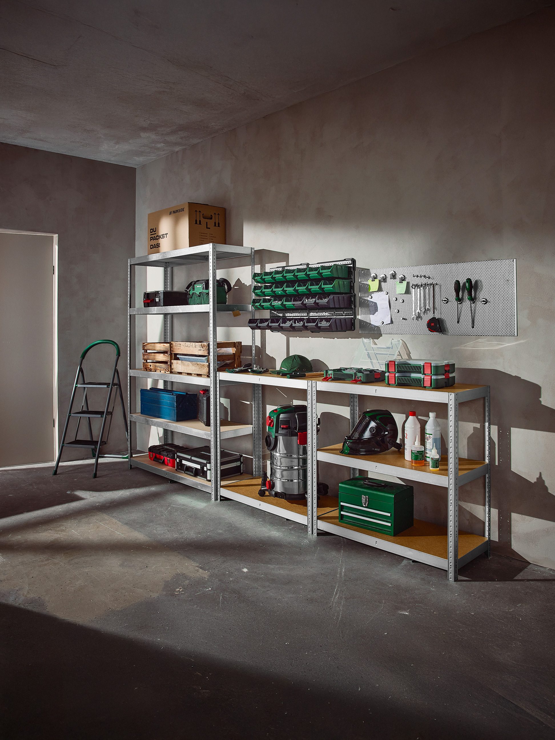 Zorganizowany garaż ze stojakami pełnymi narzędzi, pojemników do przechowywania i sprzętu warsztatowego.