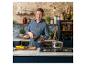 Jamie Oliver w rustykalnej kuchni, trzymający patelnię, z warzywami na blacie.
