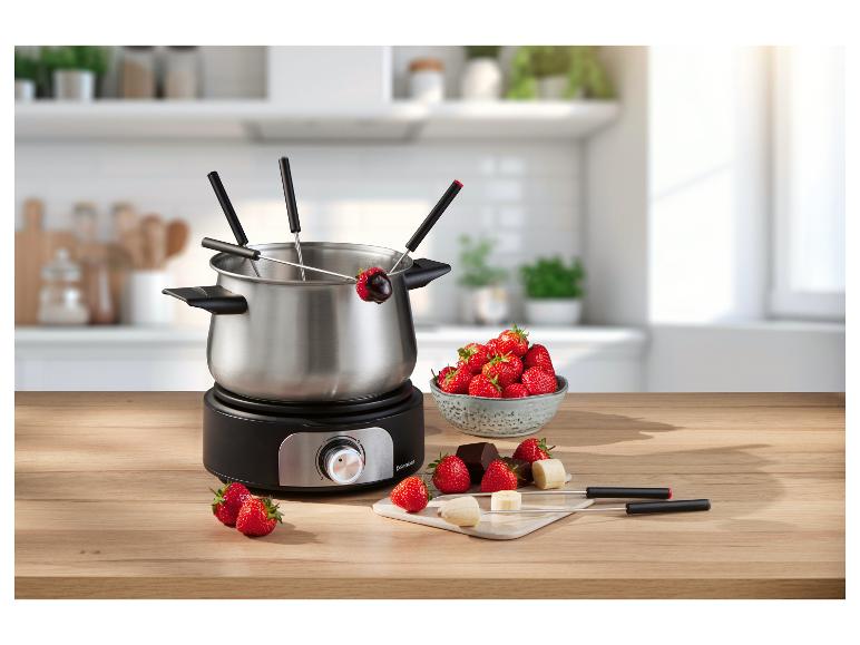 Elektryczny zestaw do fondue z truskawkami, czekoladą i bananami na drewnianym stole.