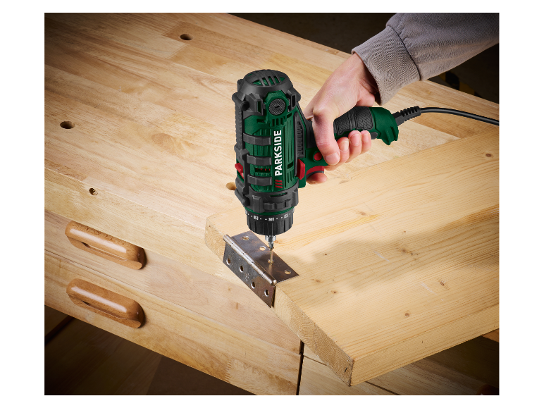 Osoba używa wiertarki Parkside do przykręcania zawiasu do drewnianej deski.