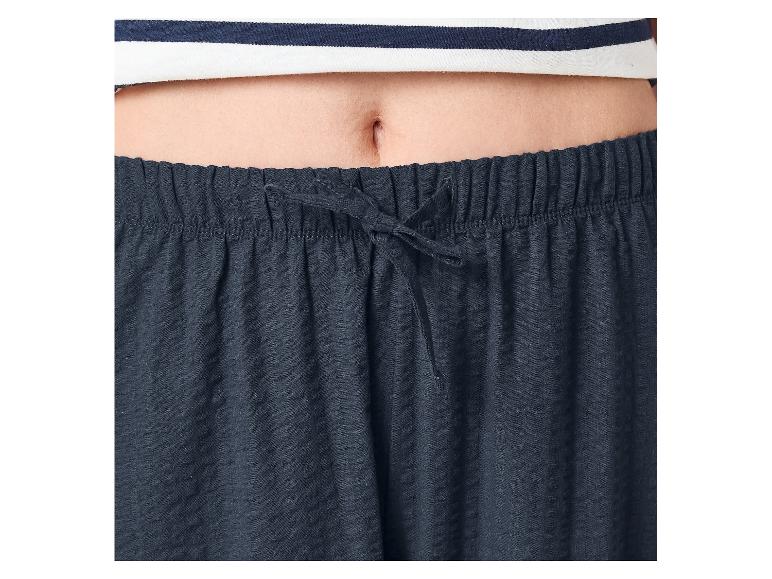 Brzuch osoby w pasiastym topie i granatowych spodniach piżamowych ze sznurkiem.