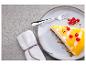 Kawałek sernika z polewą mango i czerwonymi porzeczkami na talerzu z widelcem.