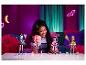 Uśmiechnięta dziewczyna trzyma lalki Monster High, z innymi lalkami i akcesoriami na stole.