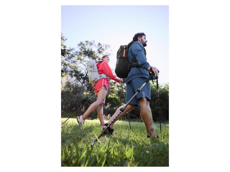 Para wędrująca z plecakami i kijkami trekkingowymi po trawiastym terenie.