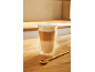 Latte macchiato w szklanej szklance i złota łyżeczka na drewnianym stole.