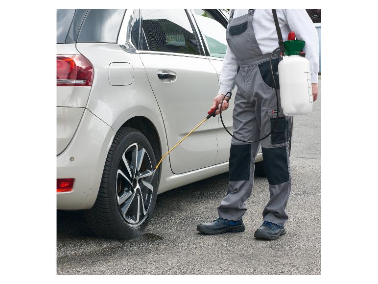 Mężczyzna w kombinezonie czyści opony samochodu za pomocą opryskiwacza ciśnieniowego.