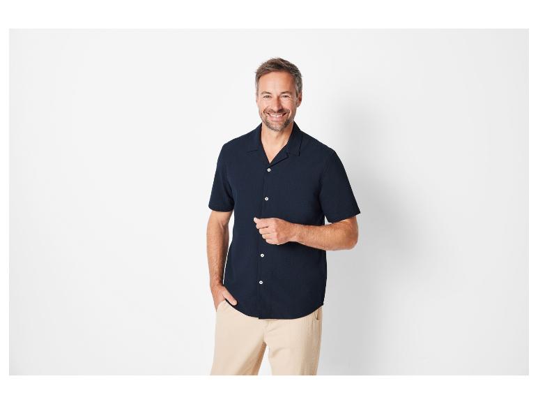 Uśmiechnięty mężczyzna w koszuli z krótkim rękawem i beżowych spodniach.