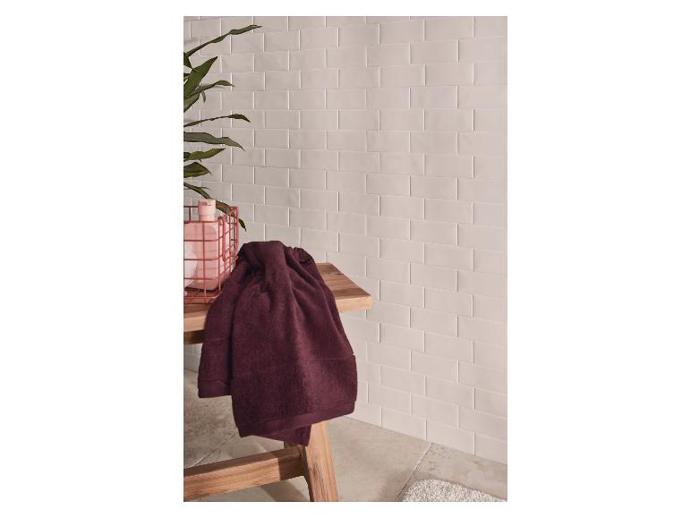 Ręczniki kąpielowe na drewnianej ławce, z kafelkowymi ścianami i rośliną.