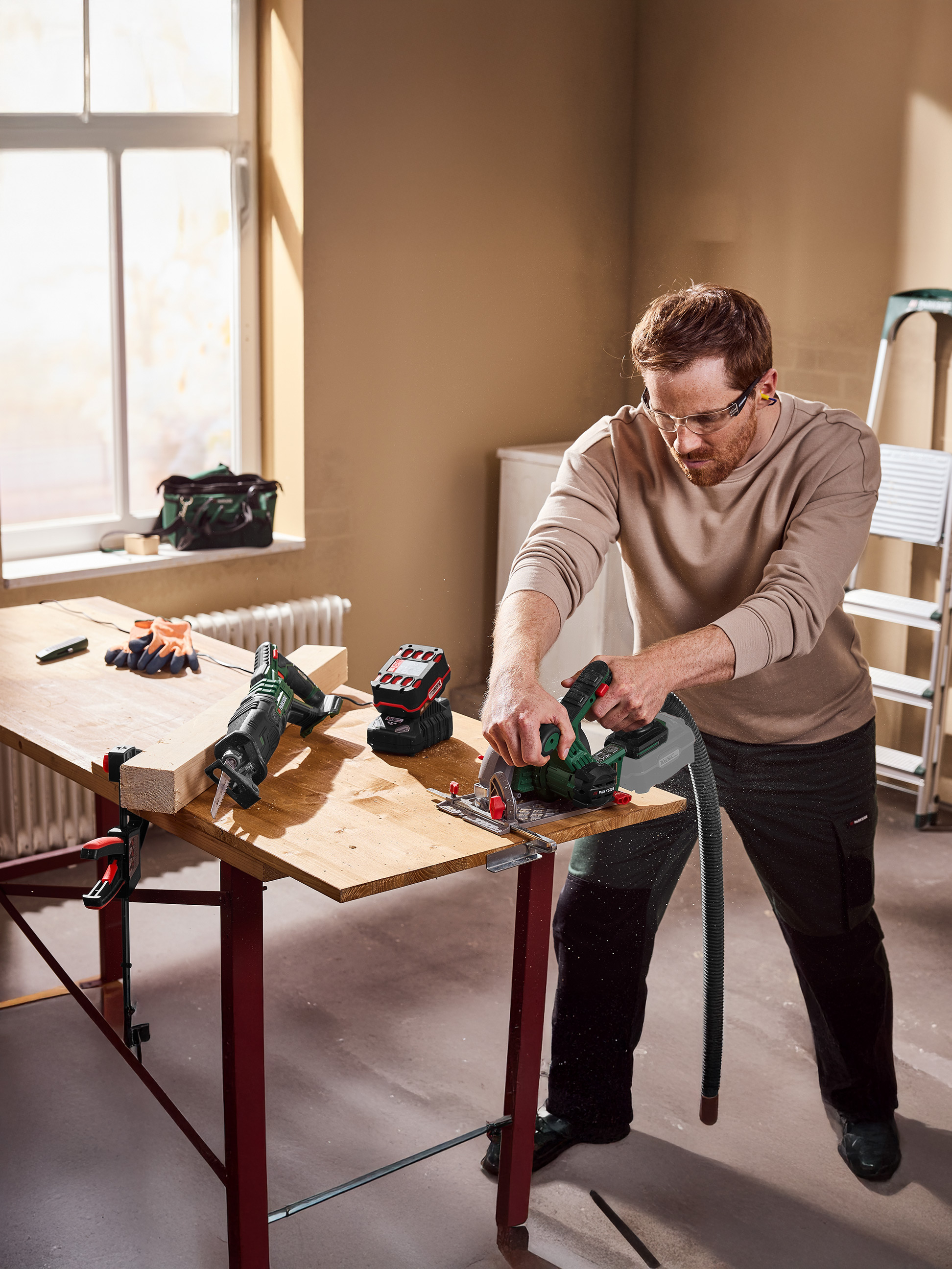 Mężczyzna używa piły tarczowej do cięcia drewna na stole warsztatowym, z piłą szablastą w pobliżu.