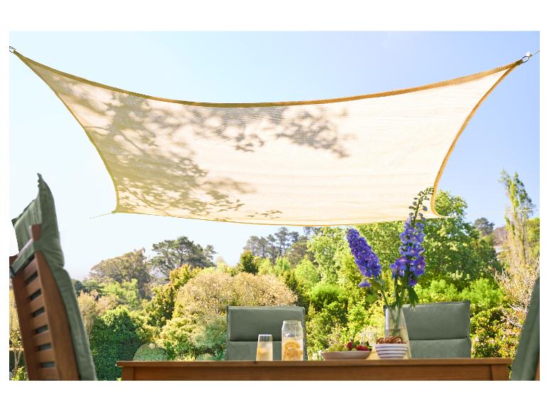 Beżowy żagiel przeciwsłoneczny nad drewnianym stołem ogrodowym z napojami i przekąskami.