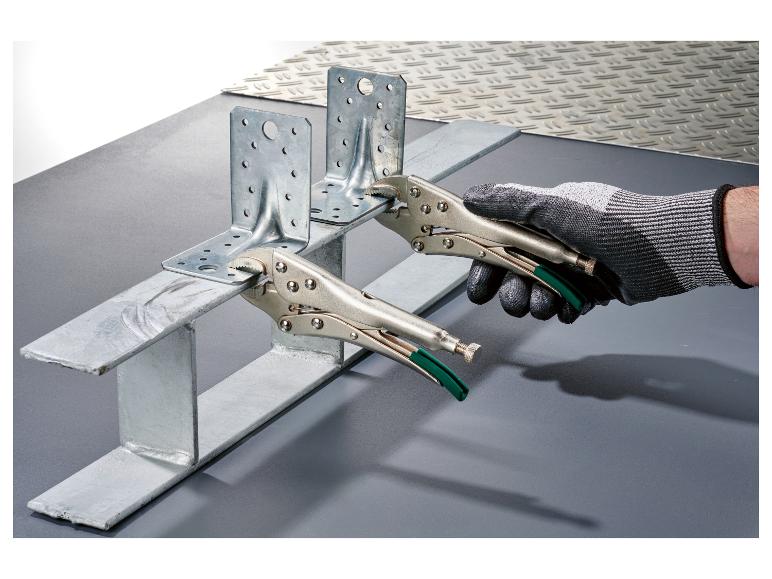 Ręka trzyma metalowy wspornik szczypcami, przymocowany do metalowego profilu.