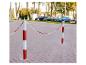 Czerwono-białe słupki z łańcuchem na ulicy z zaparkowanymi samochodami.