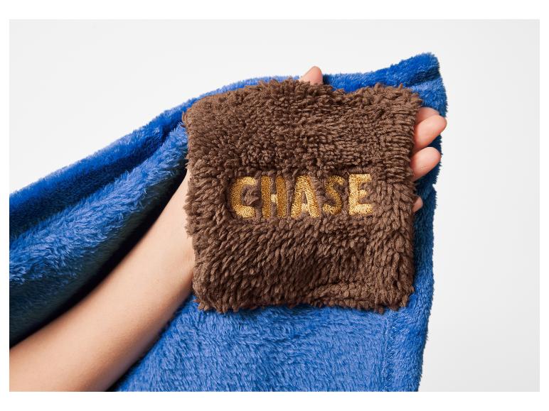 Niebieski i brązowy koc z haftowanym napisem „CHASE” trzymany w dłoni