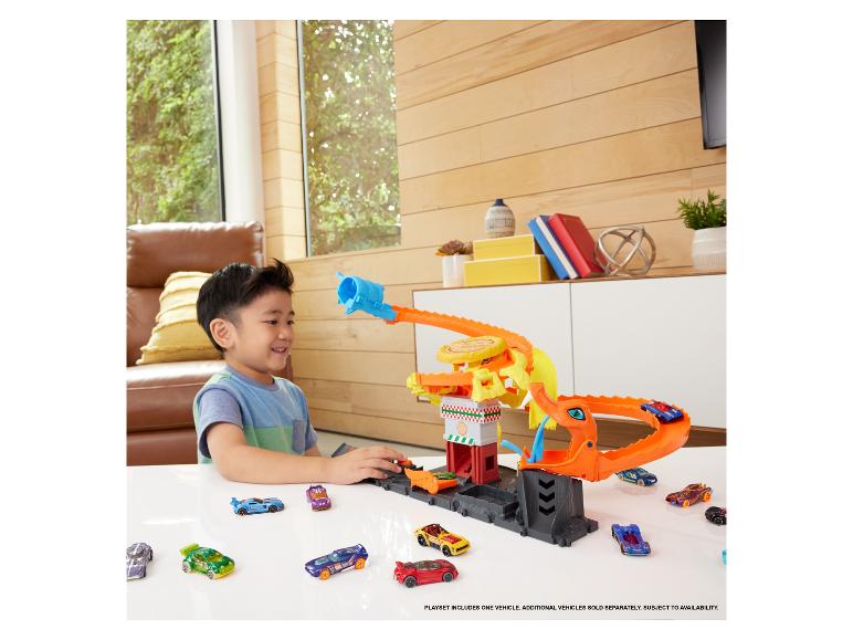 Chłopiec bawi się zestawem Hot Wheels ze smokiem i wieloma samochodami.
