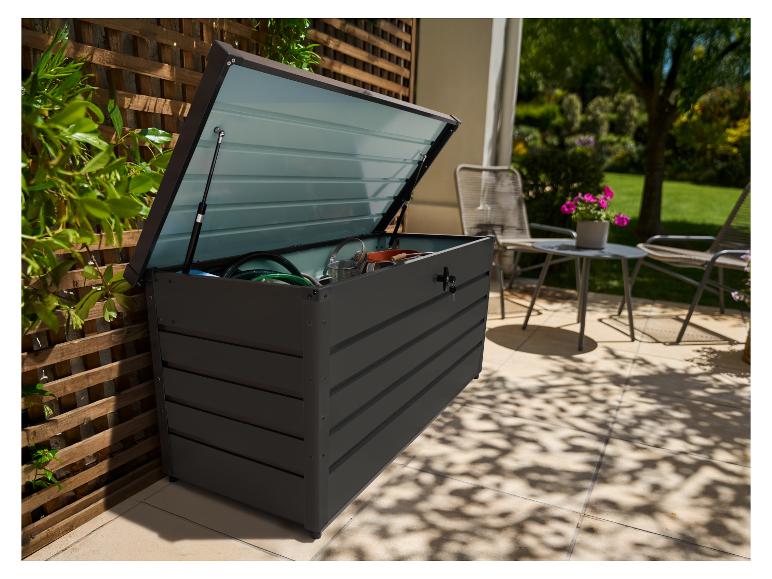 Ciemnoszara skrzynia ogrodowa z otwartą pokrywą, wypełniona narzędziami ogrodowymi, na tarasie.