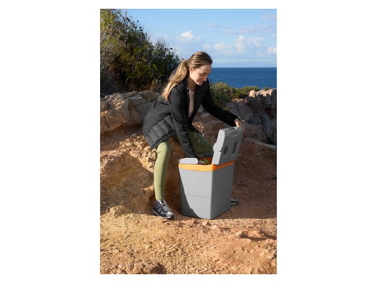 Kobieta otwiera szaro-pomarańczową lodówkę elektryczną na skalistym terenie nad morzem.