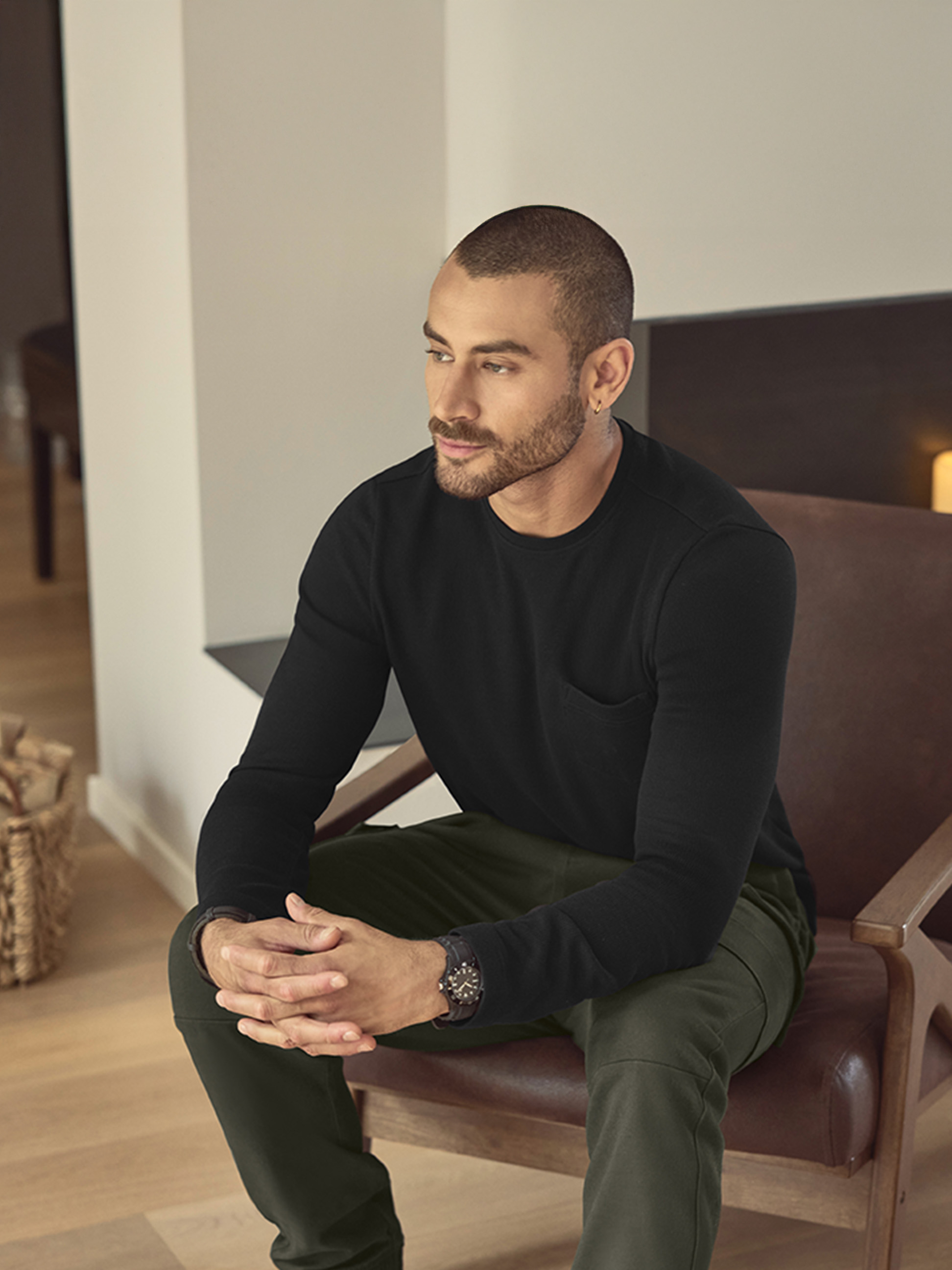 Mężczyzna w czarnej koszulce z długim rękawem i zielonych spodniach, siedzący na skórzanym krześle